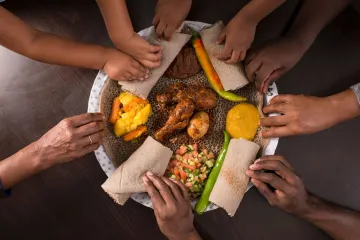 Several people sharing an Ethiopian meal and using pieces of injera to pick up the food.