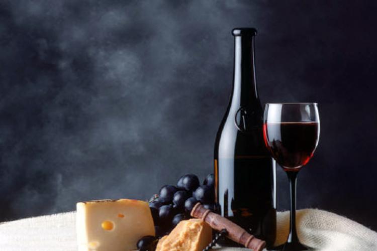 A bottle anda glass of red wine with grapes, cheese and bread.