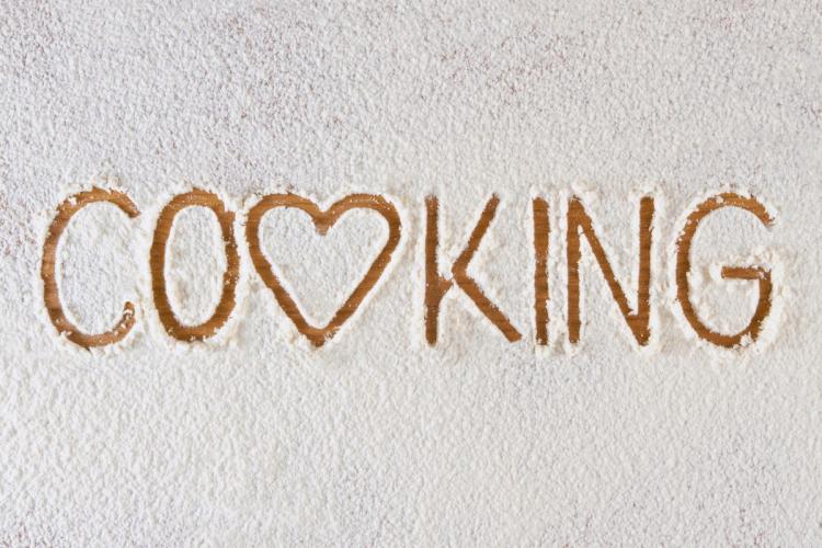 The word COOKING written in flour, with a heart symbol replacing the first 'O' to emphasize love for cooking.
