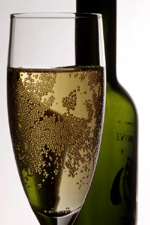 A glass of sparkling wine with a bottle in the background.