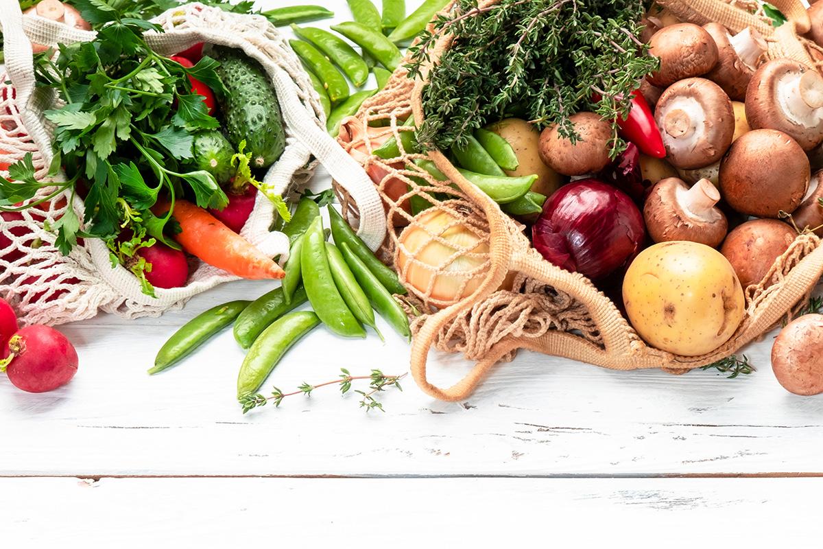 Healthy food selection: mushrooms, beans, tomatoes, avocados, and herbs. Reusable shopping textile bags full of organic spring vegetables from local farmers market.