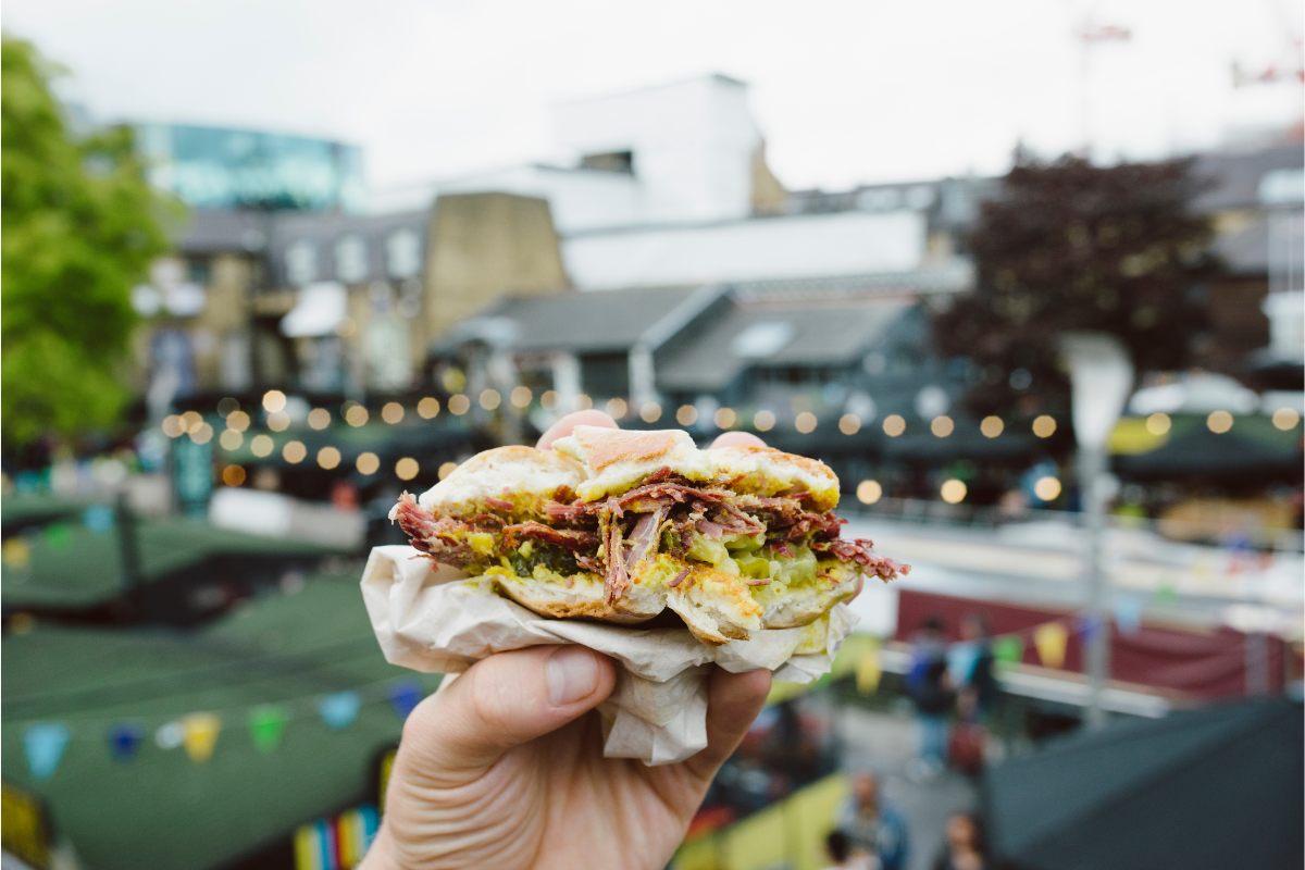 A hand holding a sandwich from a street food stall.
