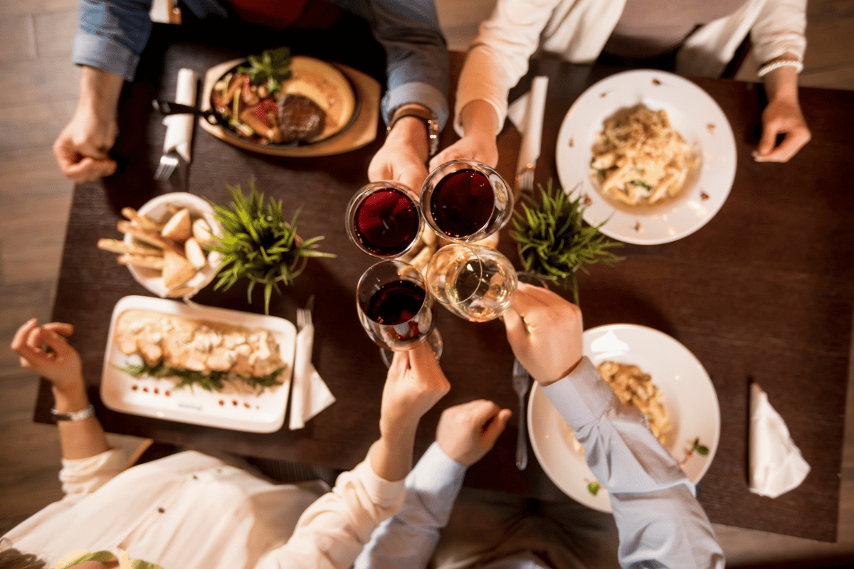 Toasting with wine over table with food.
