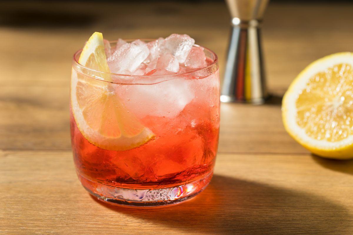 Campari spritz with ice and a lemon wedge on a wooden surface with a half lemon nearby.