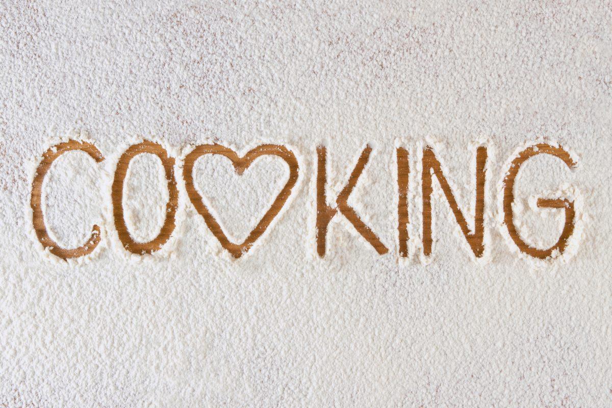 The word COOKING written in flour, with a heart symbol replacing the first 'O' to emphasize love for cooking.