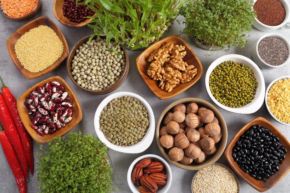 Assortment of organic seeds, nuts, and grains in bowls, including beans, lentils, walnuts, and fresh herbs.