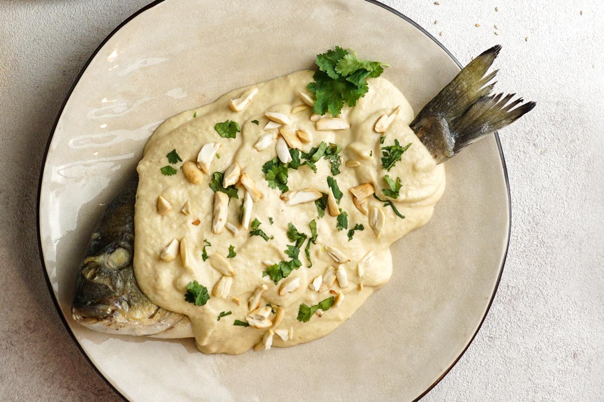 Whole fish covered in tahini sauce, garnished with chopped almonds and fresh parsley.