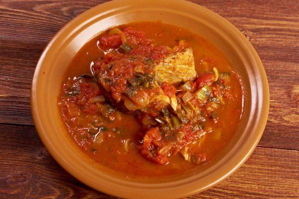 A plate of hraime, a traditional Libyan dish, featuring a piece of fish cooked in a thick, spicy tomato sauce.