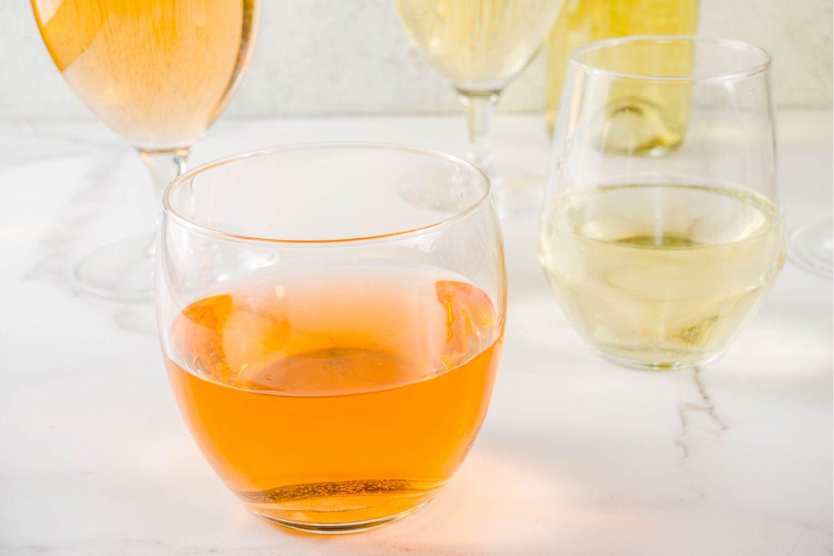 A selection of wine glasses on a table, featuring an orange wine in a stemless glass in the foreground and several glasses of white wine and one more of orange wine in the background.