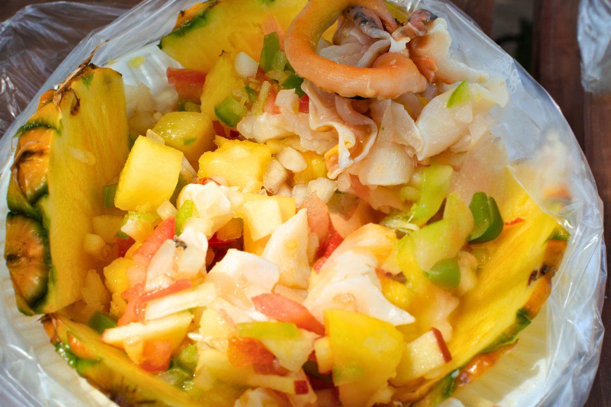 Conch salad served in a hollowed pineapple shell, featuring diced fruits, vegetables, and conch, with a vibrant and tropical appearance.