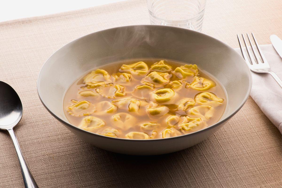 A bowl of tortellini al brodo with spoon, fork and napkin on the side.