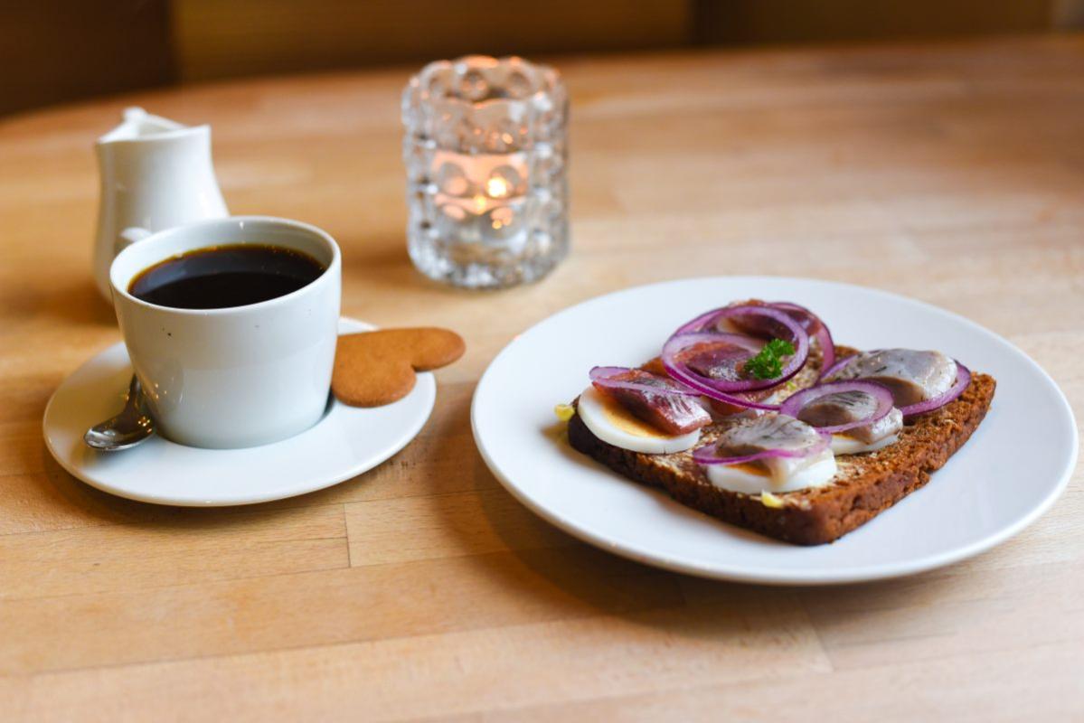 An Icelandic breakfast with an open-faced herring sandwich, black coffee, and a heart-shaped ginger cookie.