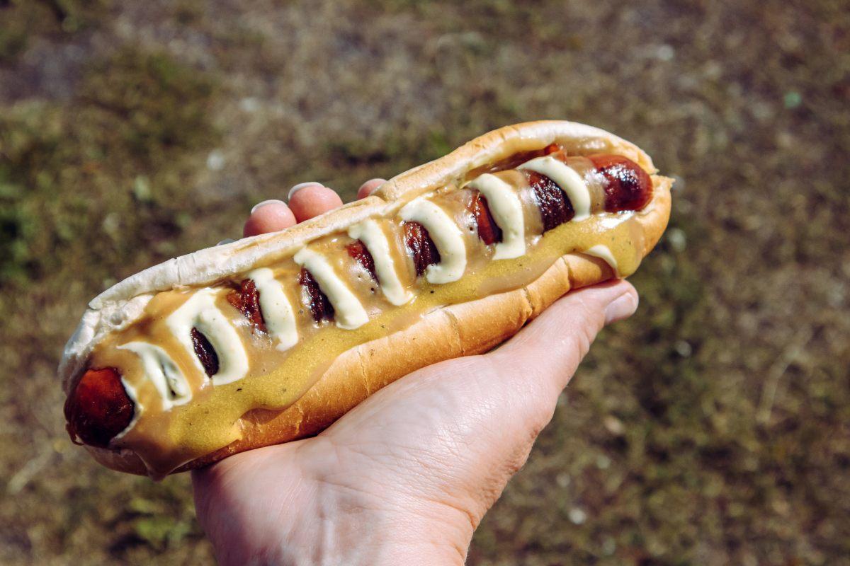 An Icelandic hot dog, known as pylsur, with mustard, remoulade, and crispy onions, held in a hand outdoors.