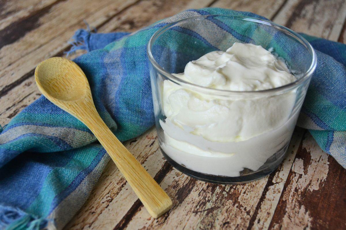 A glass filled with thick Icelandic skyr, accompanied by a wooden spoon and a blue checkered napkin on a rustic table.