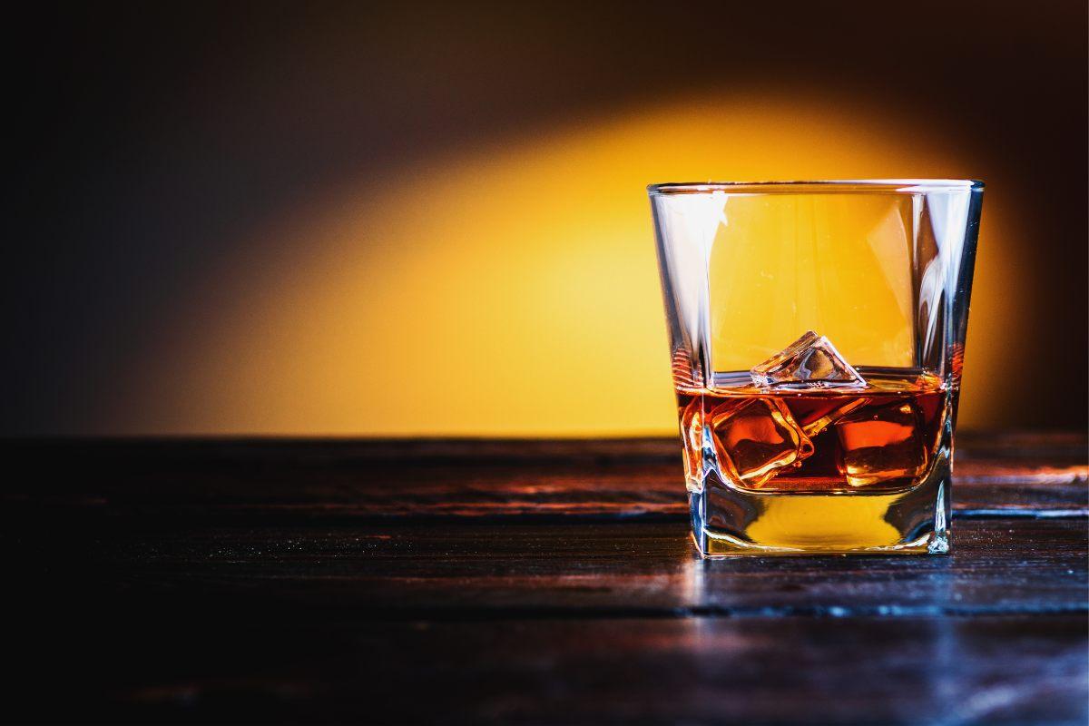 Bourbon with ice cubes on darke wood table and orange background.