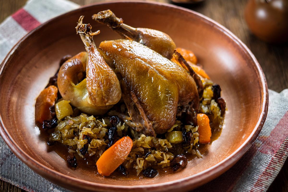 Stewe squab with cabbage, raisins and carrot plated in a stoneware dish.