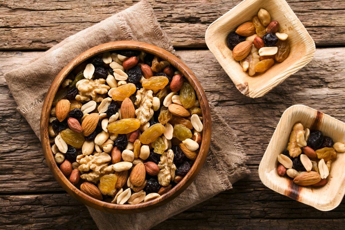 A close-up, top-down view of a rustic wooden bowl brimming with a healthy mix of nuts and dried fruit.