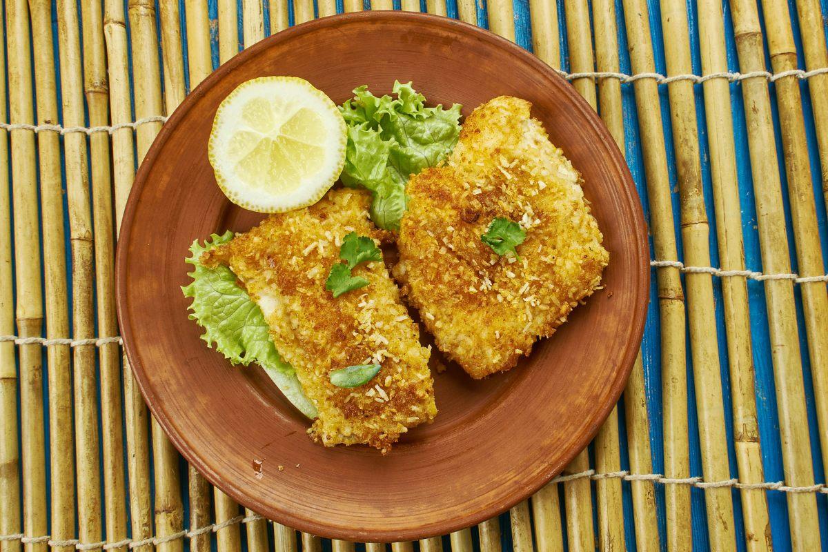 Two pieces of coconut crusted cod on a rustic plate.