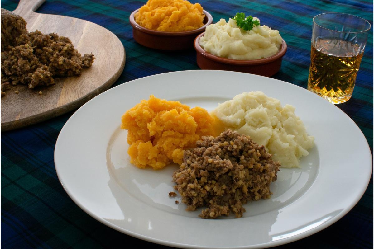 Plate of haggis, mashed rutabaga, or neeps, and mashed potatoes or tatties on tartan cloth.
