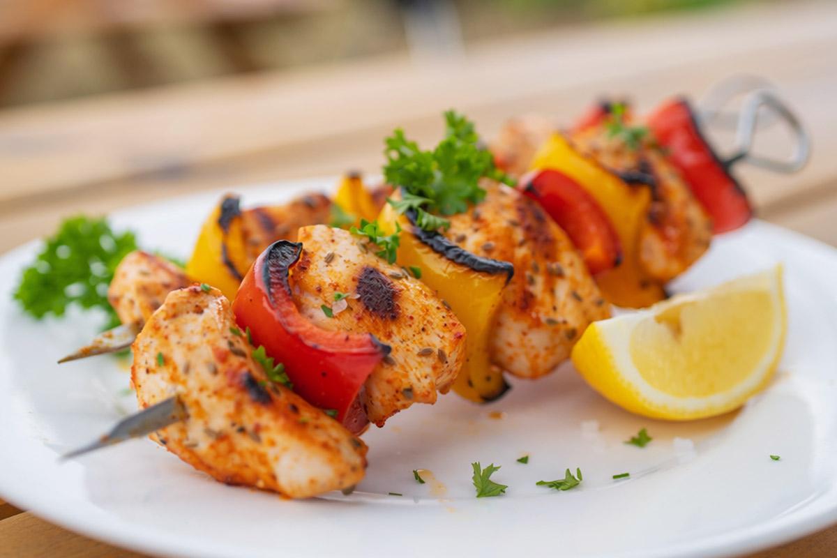A plated serving of grilled chicken and bell pepper skewers (one portion) with chicken breast cubes threaded alternately with red and yellow pepper pieces.
