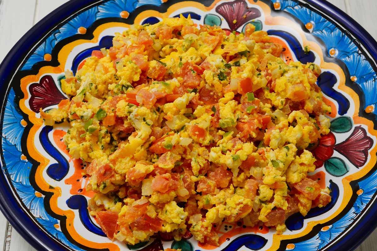 Huevos a la Mexicana or scrambled eggs, tomatoes, onions, and peppers on a decorative plate.