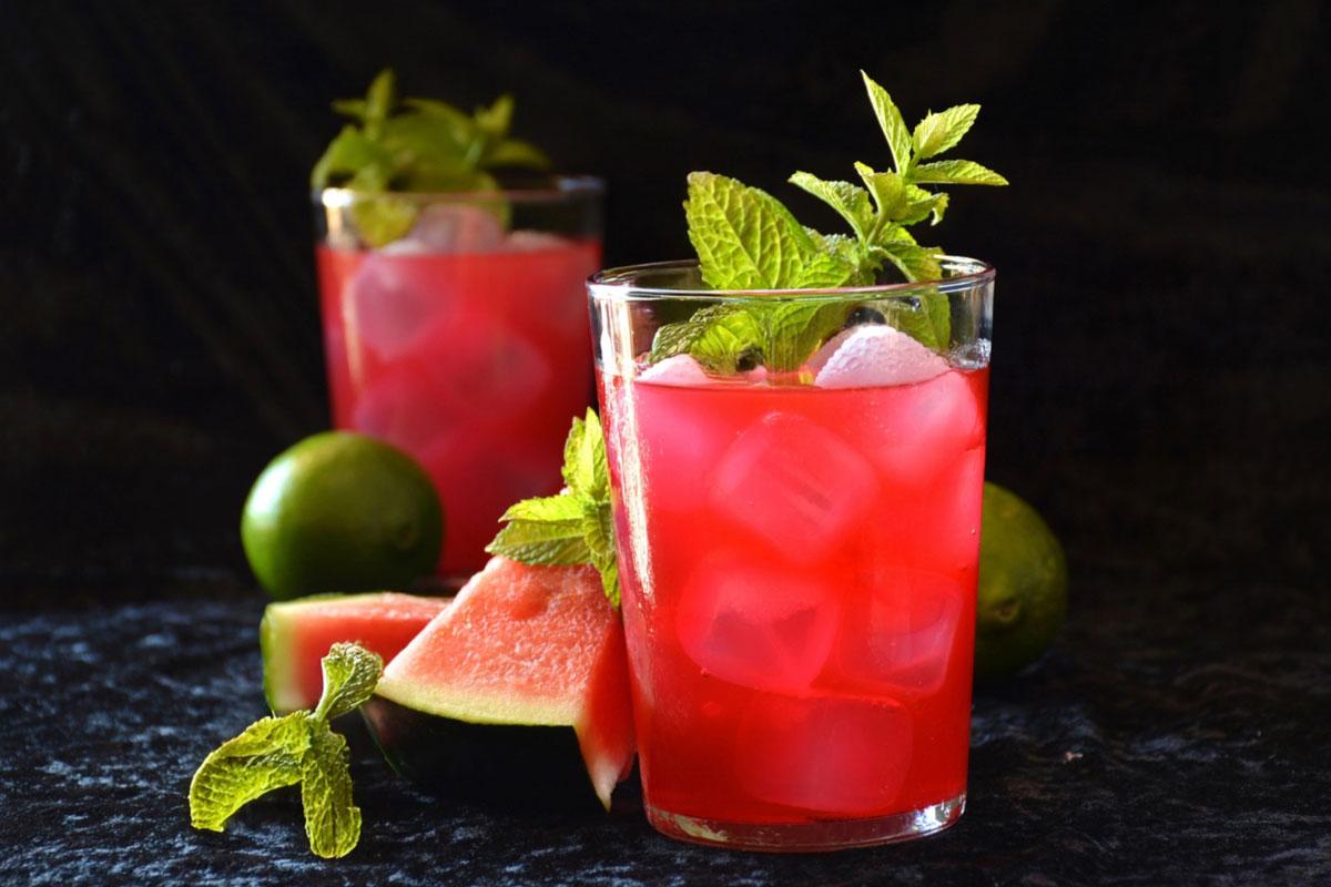 Two glasses of mint and watermelon water, or agua fresca de sandía, with ice and fresh mint, served with watermelon slices and limes.