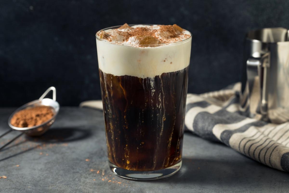 all glass of iced Einspänner topped with whipped cream and cocoa powder on a dark countertop with café-style background props.