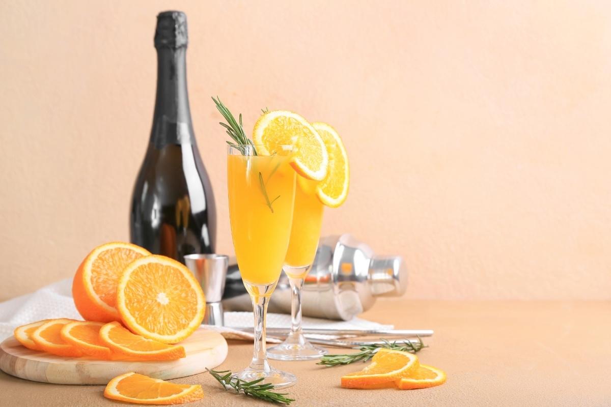 Orange mimosas with citrus garnish on a peach-toned table.