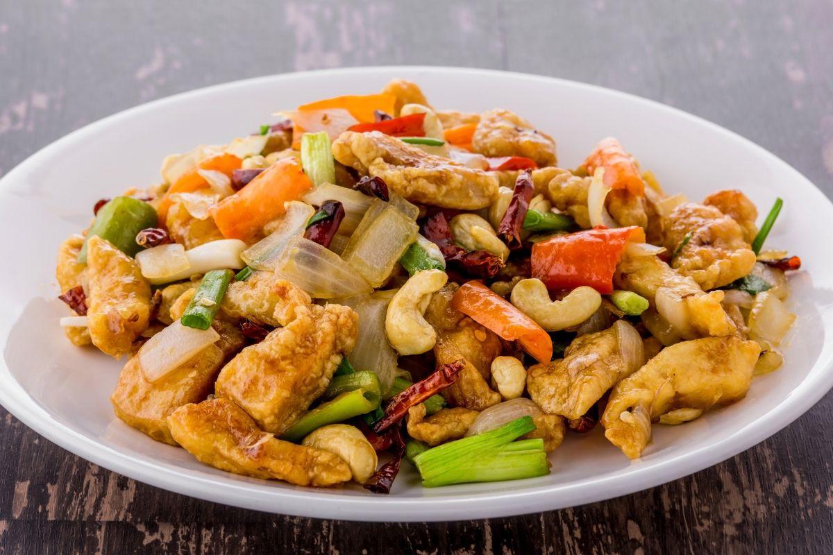 Cashew chicken stir-fry with vegetables, dried chilies, and green onions served on a white plate.