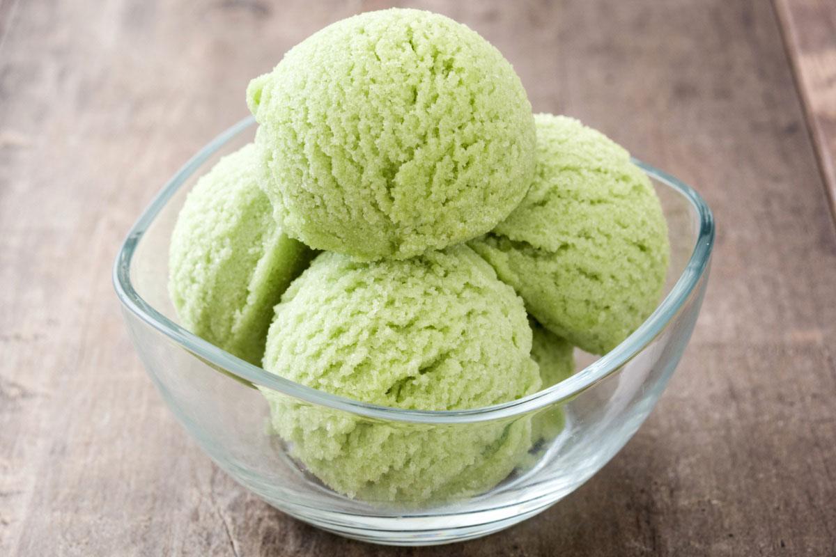 Four scoops of matcha ice cream in a glass bowl with a square rim.