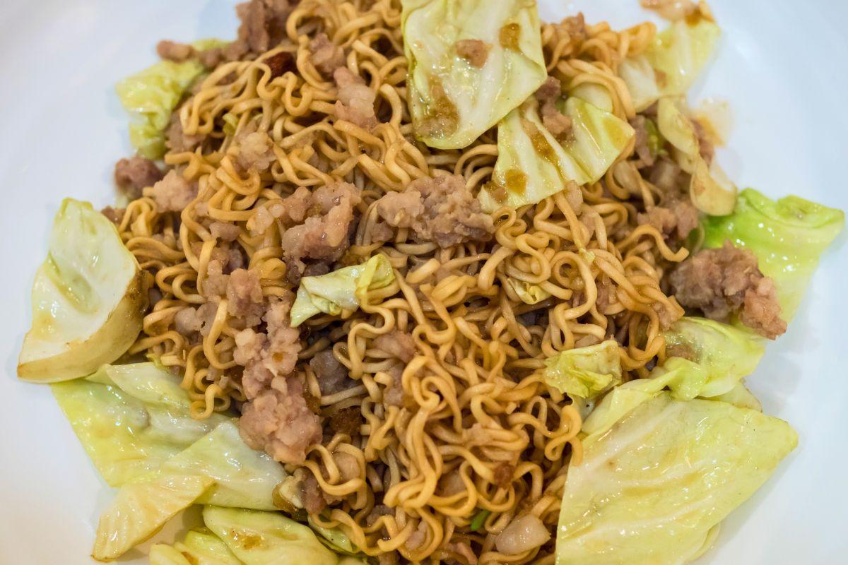 Stir-fried noodles with pork and cabbage on a white plate.