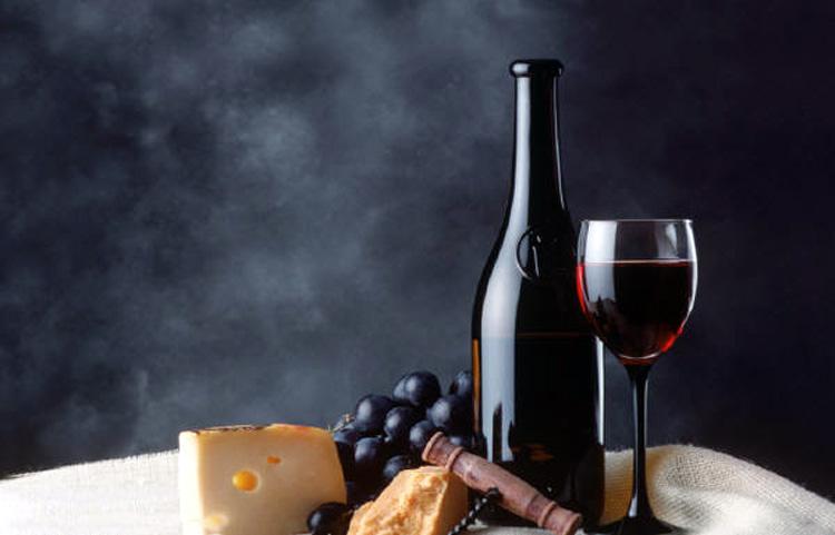 A bottle anda glass of red wine with grapes, cheese and bread.
