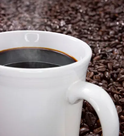 A cup with dark coffee with a background of roasted coffee beans.