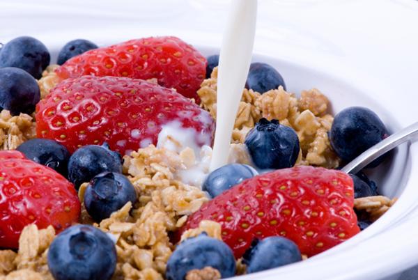Pouring milk on breakfast granola, strawberries and blueberries.
