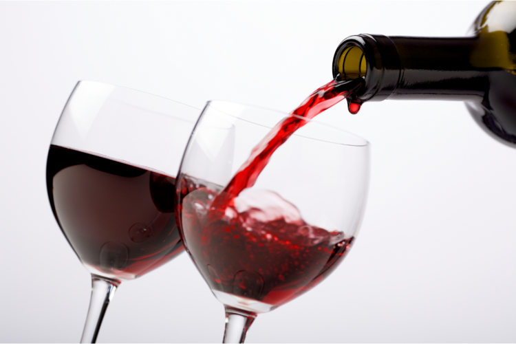 A bottle filling two wine glasses with red wine.
