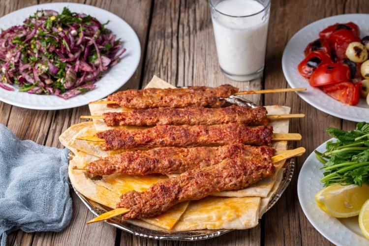 A few Adana kebabs on flat bread with accompanying dishes.