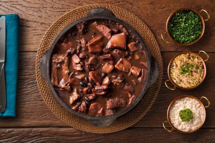 Top view of Brazilian feijoada with sides of white rice, farofa and cuve minheira.