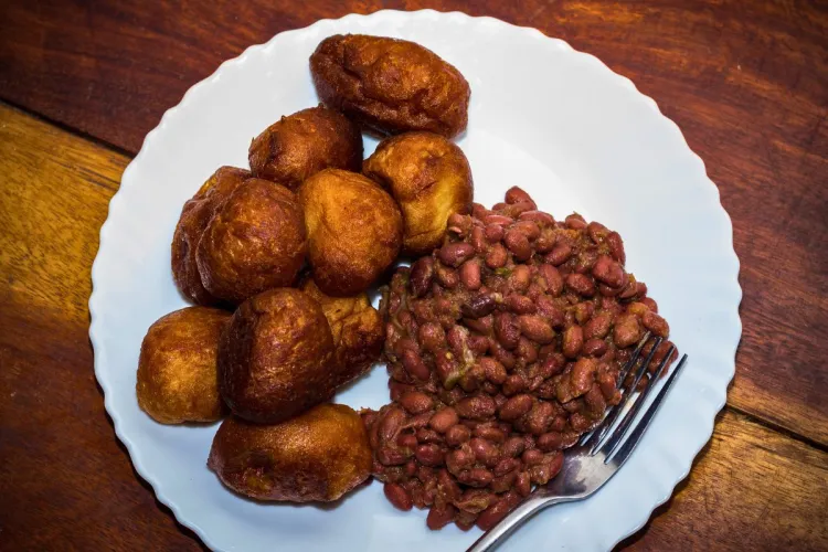 A plate of golden-brown puff-puff, or fried dough balls, served with seasoned red beans, a traditional West African dish, on a white plate with a fork resting on the side.