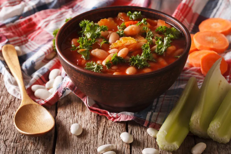 Bowl of traditional Greek Fasolada soup with white beans, carrots, celery, and parsley in a rich tomato broth, served on a rustic wooden table.