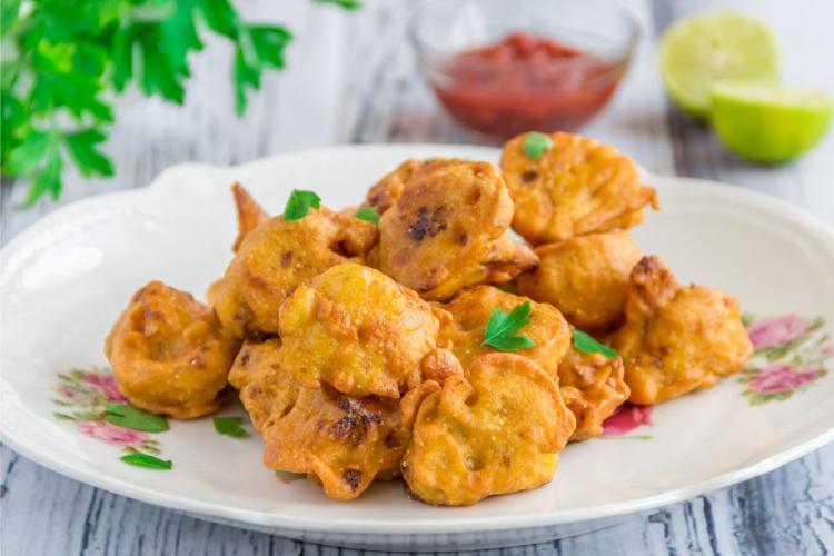 Cauliflower fritters on a floral plate with parsley and red dipping sauce in the background.