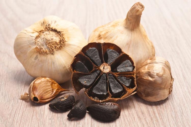 Three heads of black garlic, with one of them halved, showing the black garlic inside.