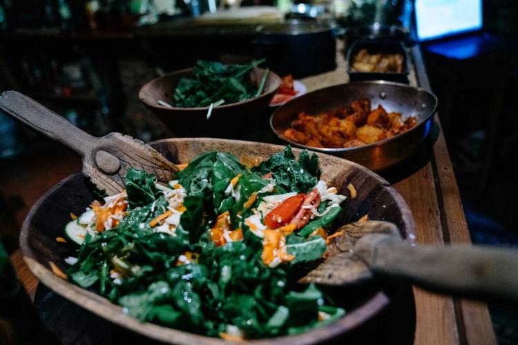 A wooden bowl with greens and other vegetables in what looks like a type of salad.