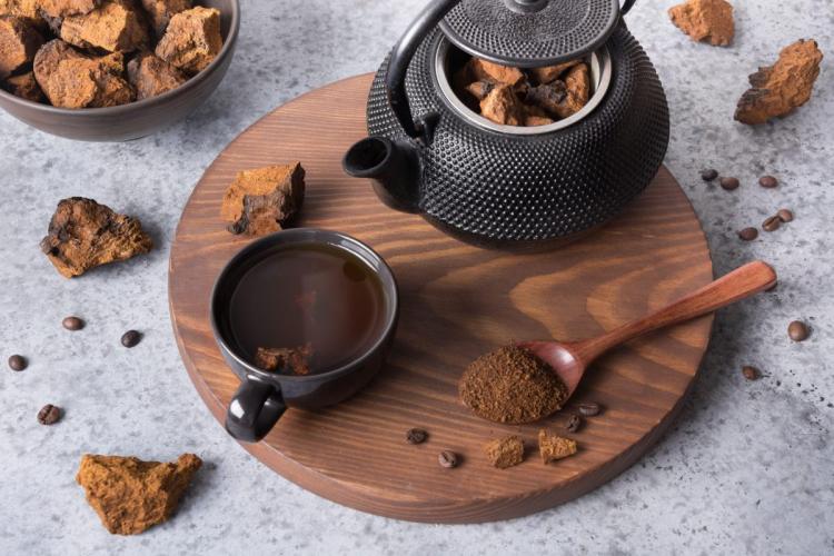 A cup of chaga mushroom tea with teapot, dried chaga chunks and powder on a wooden board.
