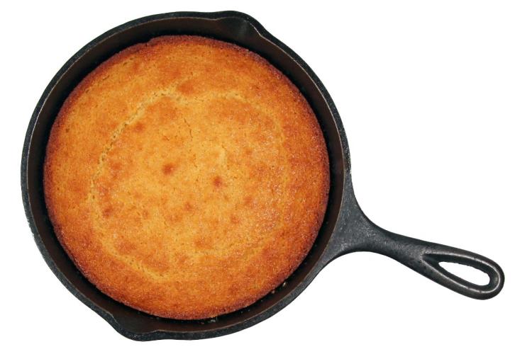 Golden-brown cornbread baked in a cast-iron skillet on a white background.