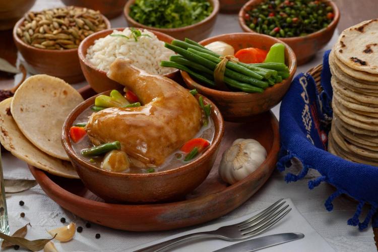 Traditional Guatemalan chicken pepián served in a clay bowl with rice, vegetables, tortillas, and assorted garnishes.
