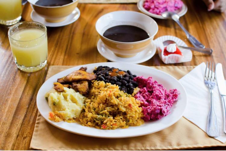 Costa Rican casado plate with rice, black beans, fried plantains, potato salad, beet salad, soup, and juice.