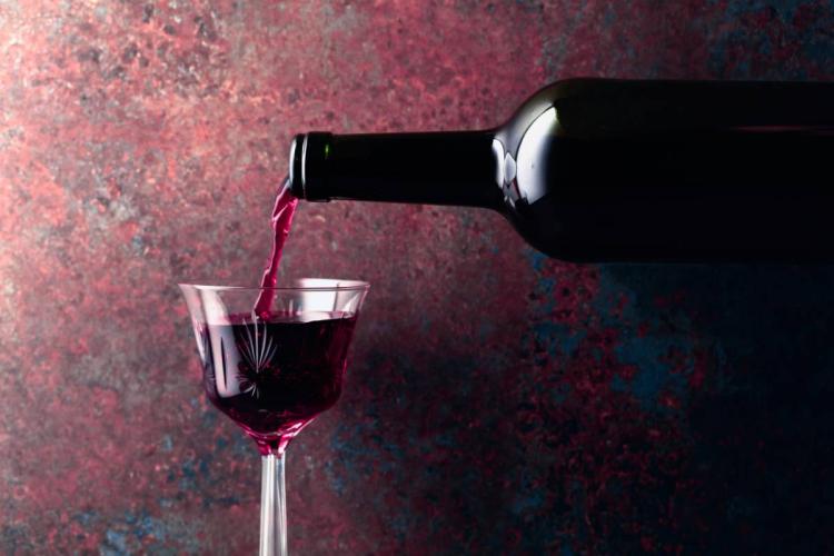 Port wine being poured from a dark bottle into a clear stemmed glass against a moody textured background.