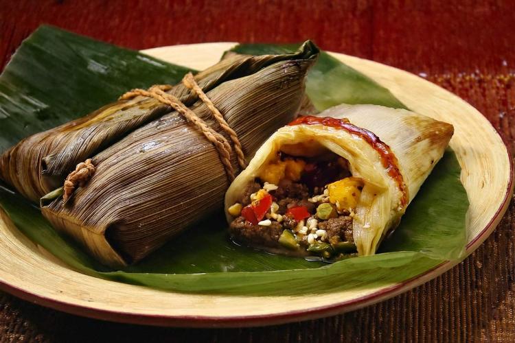 Costa Rican tamales on a banana leaf, with one tamal opened to show meat, rice, and vegetable filling.