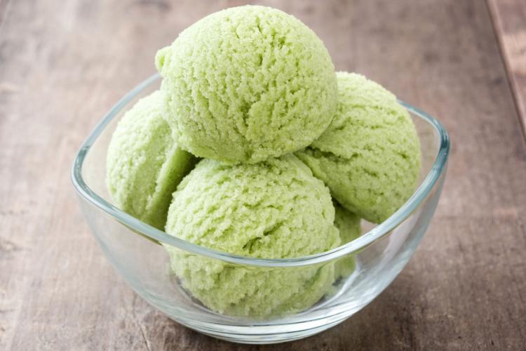 Four scoops of matcha ice cream in a glass bowl with a square rim.