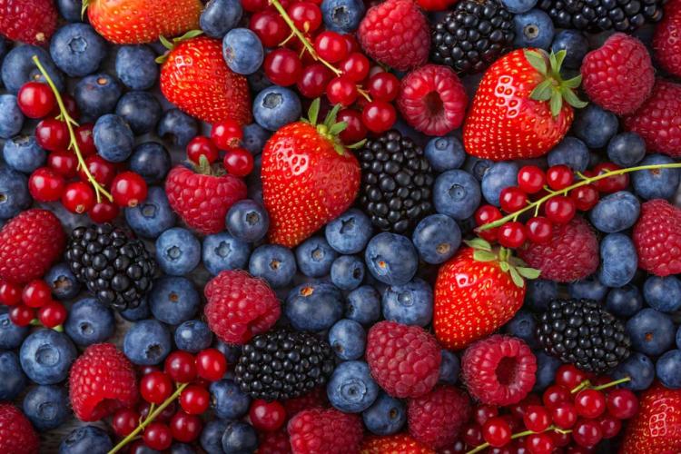 Close-up of mixed summer berries including strawberries, raspberries, blackberries, blueberries, and red currants filling the frame.